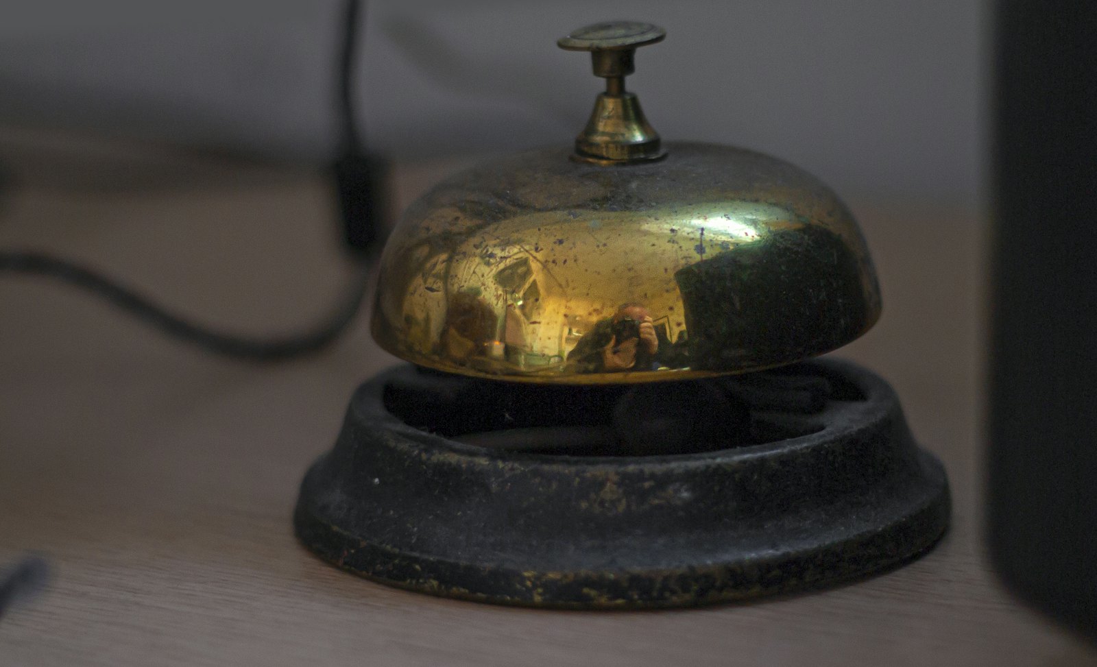 A worn brass service bell on a wooden hotel desk